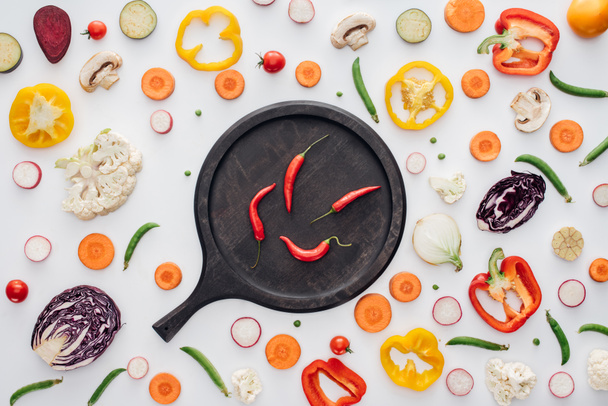 вид сверху на красный перец чили на круглой деревянной доске и свежие нарезанные овощи изолированы на белом
  - Фото, изображение