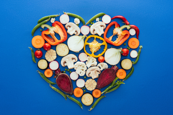 top view of various raw healthy vegetables in shape of heart isolated on blue - Foto, imagen