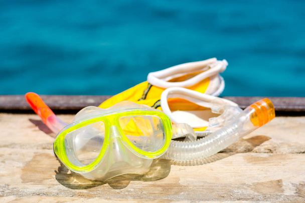 Μάσκα με αναπνευστήρα σωλήνα και ένα κίτρινο παντόφλες για κοράλλια στο φόντο της θάλασσας - Φωτογραφία, εικόνα