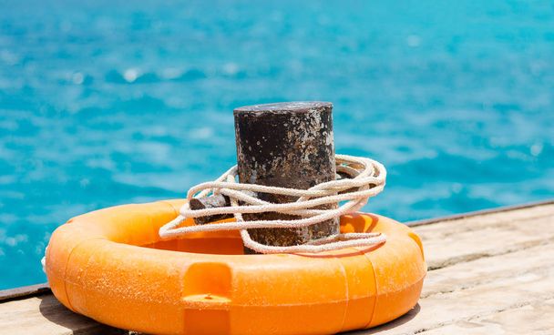 Orangefarbener Rettungsring mit Seil auf dem Hintergrund des blauen Meeres - Foto, Bild