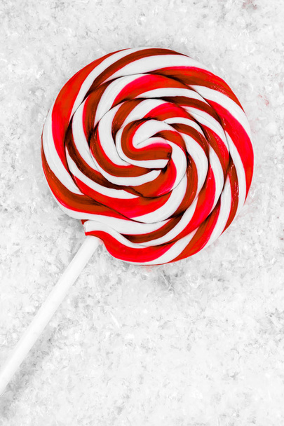 Round white and red lollipop with white stick on white artificial snow background surface - Photo, Image