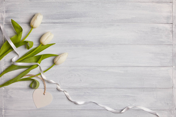 Piękne białe tulipany na drewnianym tle. Kopiuj przestrzeń. Biała wstążka.  - Zdjęcie, obraz