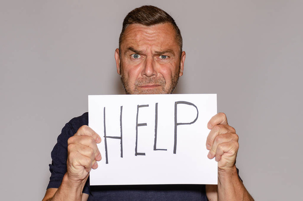 Hombre de mediana edad asustado sosteniendo hoja de papel con letras de ayuda contra fondo blanco
 - Foto, imagen