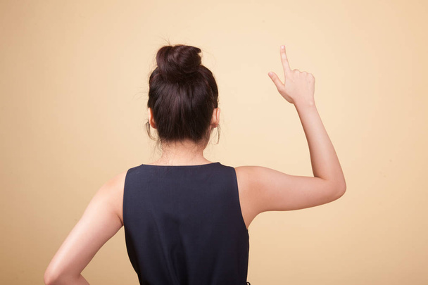 Back of Asian woman touching the screen with her finger  on beige background - Foto, afbeelding