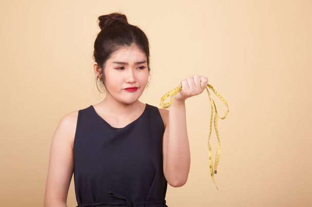Unhappy young Asian woman with measuring tape  on beige background - Photo, image
