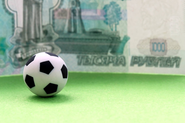 geringe Schärfentiefe. ein Fußball auf einer grünen Wiese vor dem Hintergrund einer russischen Banknote im Wert von tausend Rubel. Geld WM, das Gehalt von Spielern und Trainern, Sportwetten. - Foto, Bild