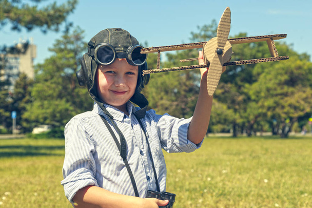 Das Konzept eines Traums ist es, Pilot zu werden, Junge in Form eines Flugzeugpiloten; Glückliches Kind im Helm mit Brille und Fernglas, das mit einem Spielzeugflugzeug spielt. gemildert - Foto, Bild