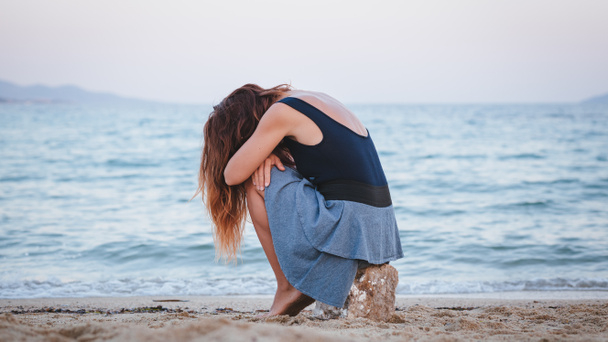 Mulher sozinha e deprimida sentada na praia
 - Foto, Imagem