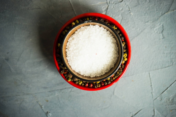 Tazón de cerámica rústico con sal marina saludable y diferentes tipos de maíz pimienta sobre fondo de hormigón con espacio para copiar
 - Foto, imagen