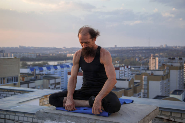 A middle-aged man is engaged in yoga on the roof. Yoga on the roof at sunset. - Foto, Bild