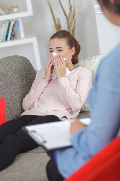 young woman blowing nose with napkin and doctor at home - Photo, Image