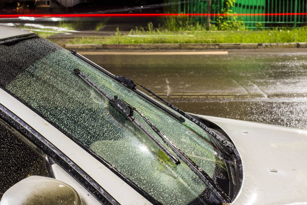красивые капли воды на лобовое стекло автомобиля с включенными стеклоочистителями, во время грозы и дождя в ночном городе. передний и задний фон размыт
 - Фото, изображение