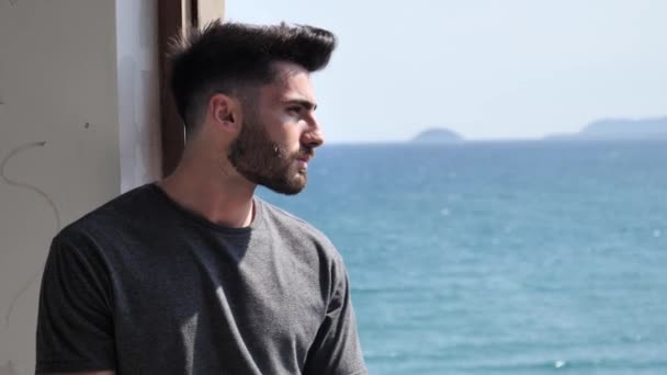 Young man leaning against window with sea behind - Imágenes, Vídeo