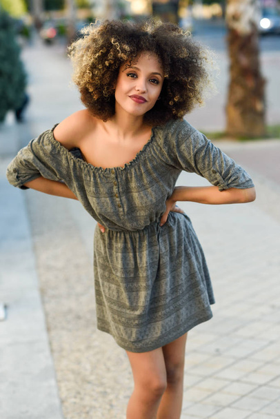 Mujer joven mixta con peinado afro sonriendo en el fondo urbano. Chica negra vistiendo ropa casual
. - Foto, Imagen