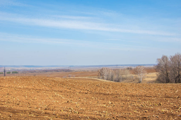 Spring landscape. Freshly plowed field. hilly terrain. trees without leaves. Multicolored spring trees. Snow left over from last year's winter. The last snow. - Photo, Image
