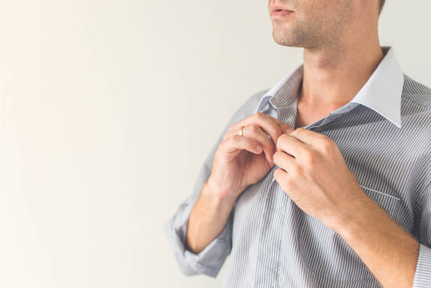 Vértes egy fiatal férfi kezét, rögzítő egy gomb az ingét. Elszigetelt fehér background - Fotó, kép