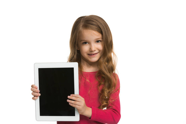 Little funny girl with tablet on white studio background. She showing something and pointing at screen. - Valokuva, kuva