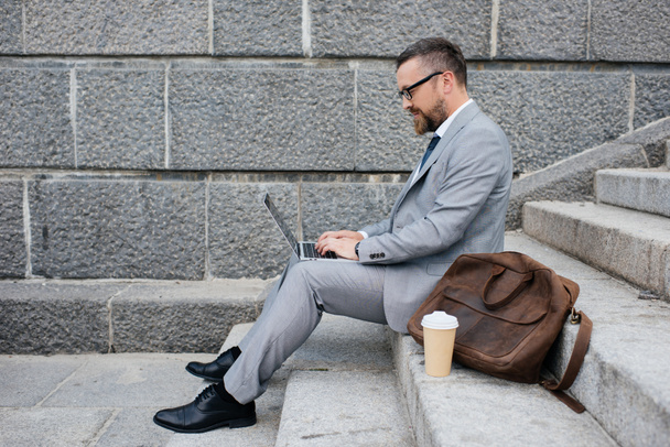επιχειρηματίας με δερμάτινη τσάντα χρησιμοποιώντας φορητό υπολογιστή και να κάθομαι στις σκάλες - Φωτογραφία, εικόνα