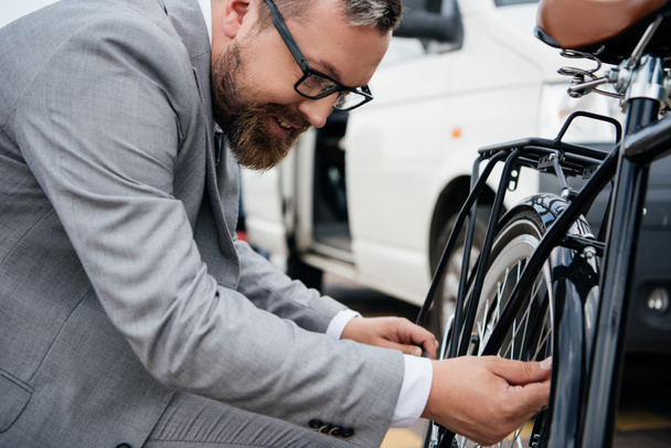 parrakas liikemies puvussa korjaamassa polkupyörän pyörää
 - Valokuva, kuva