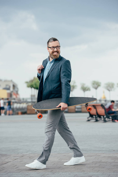 handsome bearded man with longboard walking in city - Photo, Image