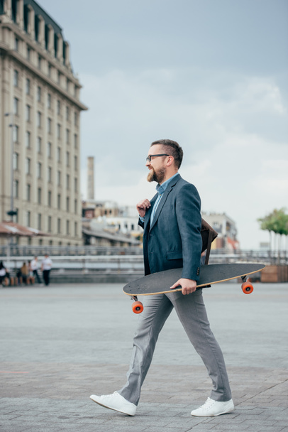 stylish handsome bearded man with skateboard walking in city - Фото, зображення