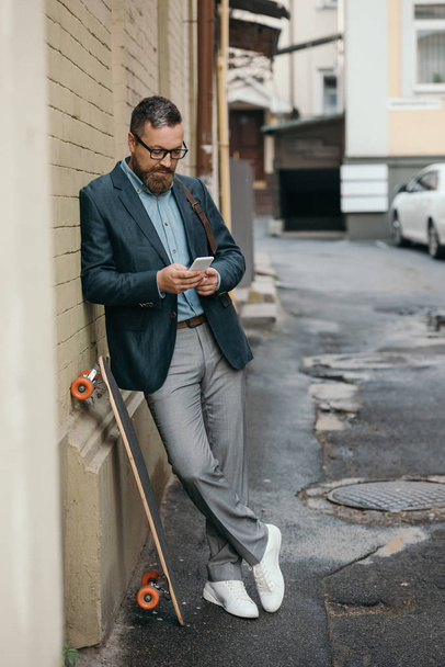 homme barbu avec longboard en utilisant un smartphone en ville
 - Photo, image