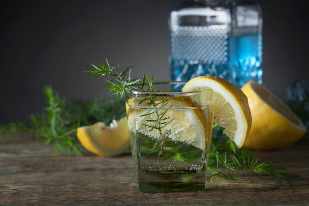 Gin blu, tonico e fette di limone su un vecchio tavolo di legno. Cocktail alcolico con fette di limone e ramo di ginepro
. - Foto, immagini
