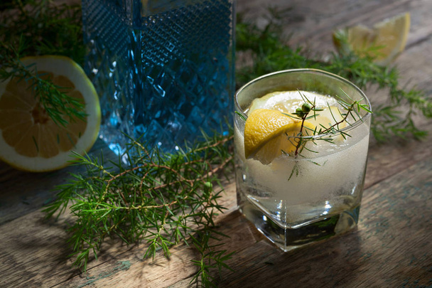 Blue Gin Tonic und Zitronenscheiben auf einem alten Holztisch. alkoholischer Cocktail mit Zitronenscheiben und Wacholderzweig. - Foto, Bild