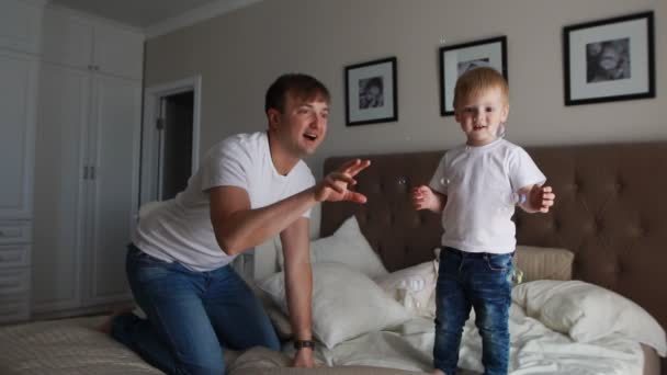 Dad plays with his son in the bedroom catching soap bubbles smiling and laughing - Footage, Video