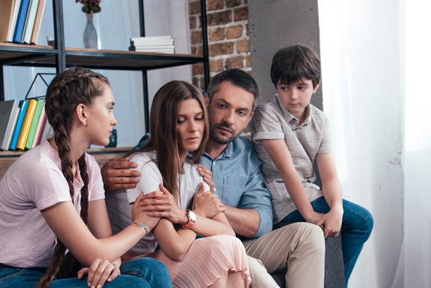 family embracing and cheering up frustrated woman on sofa in counselor office  - Photo, image