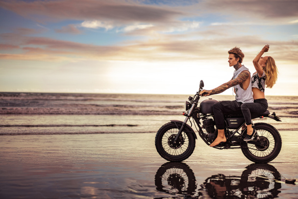 вид сбоку пары, катающейся на мотоцикле на океанском пляже
  - Фото, изображение