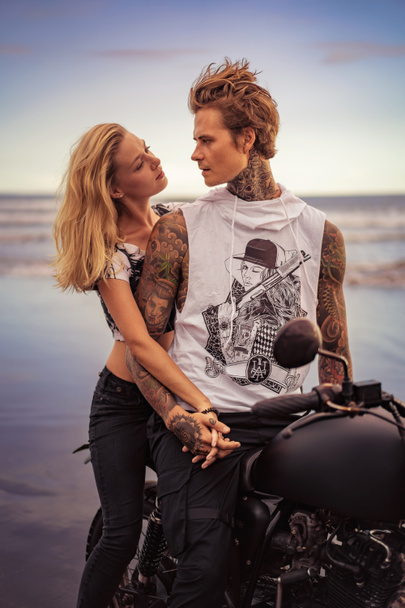 couple holding hands and looking at each other near motorcycle on ocean beach  - 写真・画像