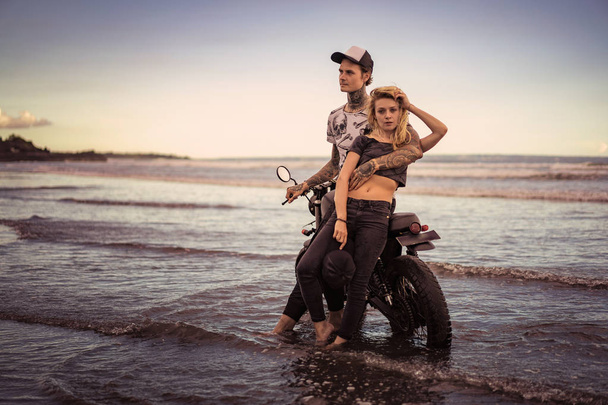 стильная пара, стоящая возле мотоцикла на берегу океана
  - Фото, изображение