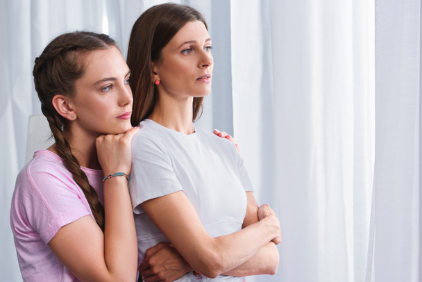 side view of daughter embracing worried mother from behind at home  - Photo, Image