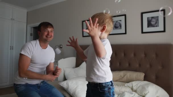 Isä leikkii poikansa kanssa makuuhuoneessa kiinni saippuakuplia hymyillen ja nauraen
 - Materiaali, video