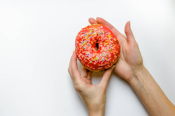 Mão feminina segurando donut rosa com polvilhas calorias extras gordura fast food excesso de peso insalubre no fundo amarelo
 - Foto, Imagem