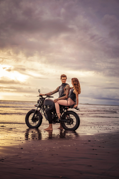 boyfriend and girlfriend sitting on motorcycle at sandy beach  - Fotó, kép