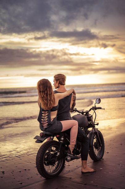back view of boyfriend and girlfriend sitting on motorbike on seashore during beautiful sunrise  - Valokuva, kuva