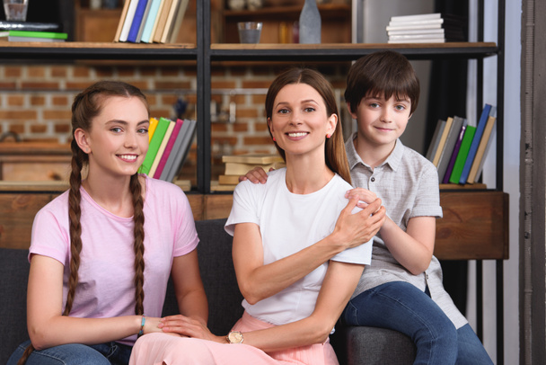 happy mother sitting on couch between son and daughter at home  - Фото, изображение