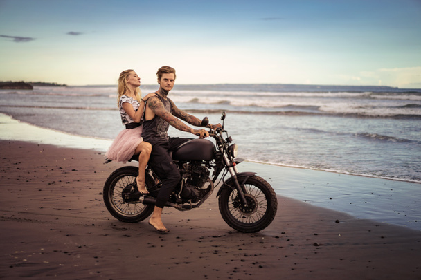 пара, сидящая на мотоцикле на берегу моря во время прекрасного восхода солнца
  - Фото, изображение