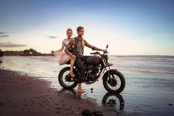 пара сидить на мотоциклі на березі моря протягом гарний схід сонця  - Фото, зображення