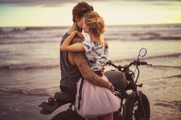 intohimoinen pari halaus moottoripyörä valtameren rannalla aikana kaunis auringonnousu
  - Valokuva, kuva