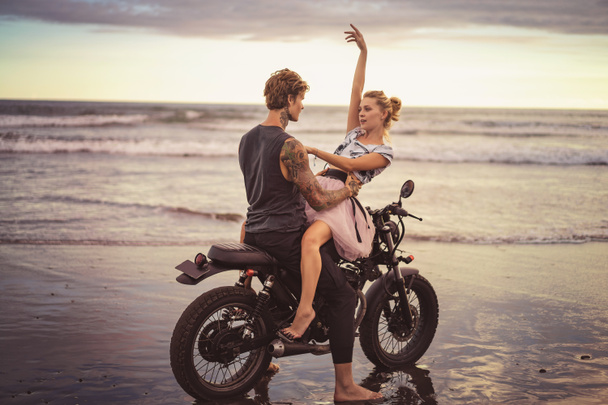 Młoda para przytulanie na motocykl na ocean plaża podczas piękny wschód słońca  - Zdjęcie, obraz