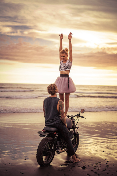happy girlfriend standing on motorcycle with hands up on ocean beach  - Photo, image