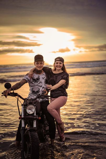 smiling couple with motorcycle on ocean beach  - Фото, зображення