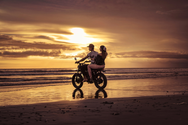 couple riding motorcycle into ocean during sunrise - Photo, Image