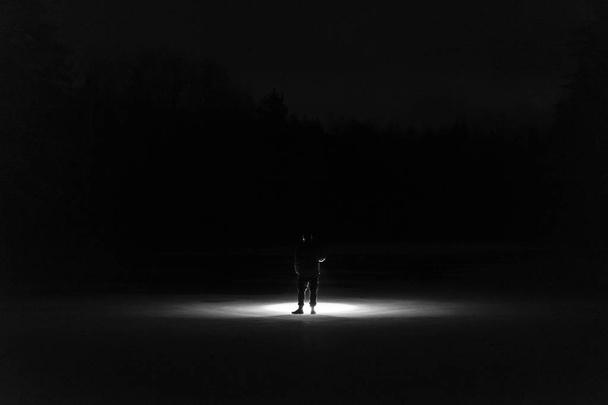 Man standing outdoor at night in forest shining forward with flashlight. Nice strong light beam. Beautiful abstract photo. Calm, peaceful and mystical image. - Photo, Image