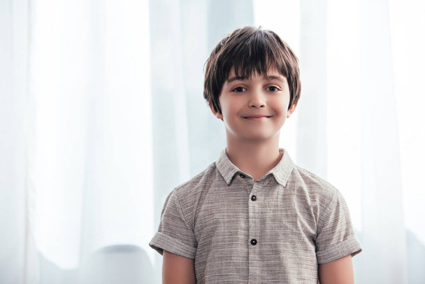 portrait of smiling little boy looking at camera in front of curtains at home  - Foto, Bild