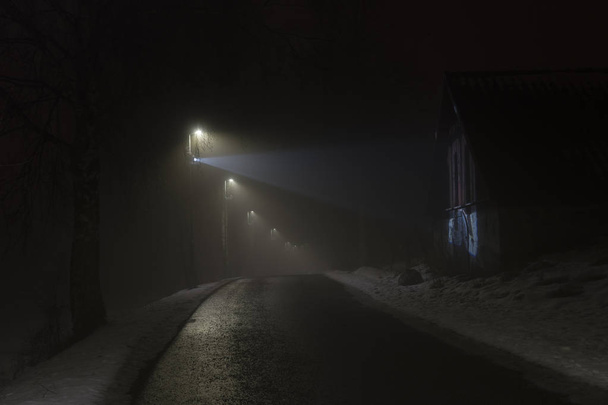 Mistige nacht in Zweden Scandinavië Europa. Prachtige, mystieke en abstracte foto van donkere winteravond met nevel in de lucht. Kalm, rustig buiten beeld met verlichting, lampen en weg. - Foto, afbeelding