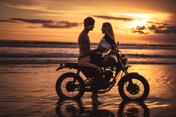 aistillinen pari halaa moottoripyörällä rannalla auringonlaskun aikana
 - Valokuva, kuva